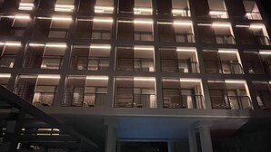 A modern building with a pool in the foreground and a series of illuminated windows on the upper floors.