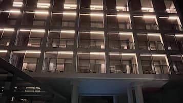 A modern building with a pool in the foreground and a series of illuminated windows on the upper floors.