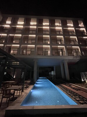 A modern building with a pool in the foreground and a series of illuminated windows on the upper floors.