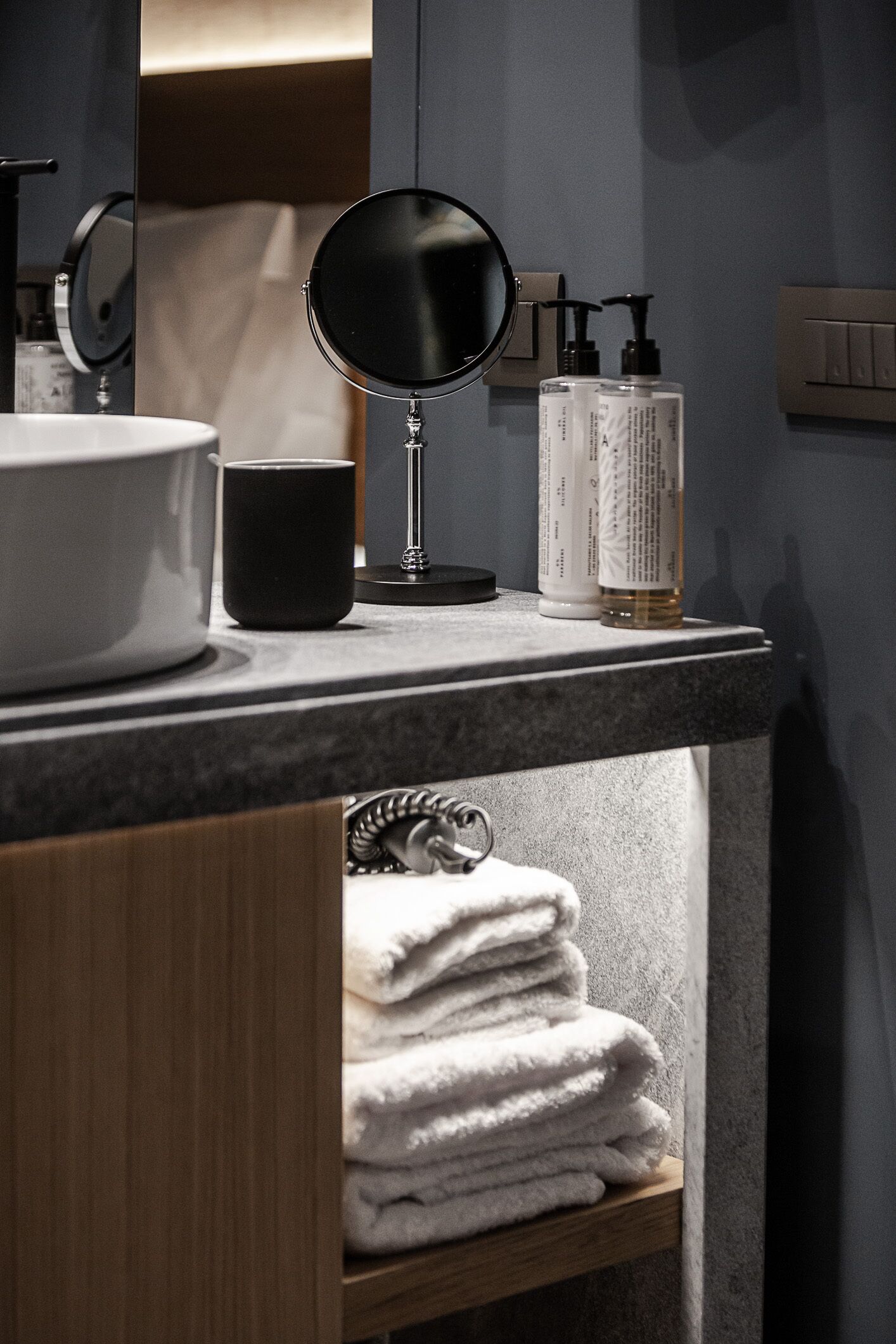 A bathroom vanity with a round mirror, a sink, a black mug, and toiletries.