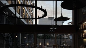 A modern restaurant with a long counter, multiple seating areas, and a view of the cityscape through large windows. - Magnes Hotel (Volos)