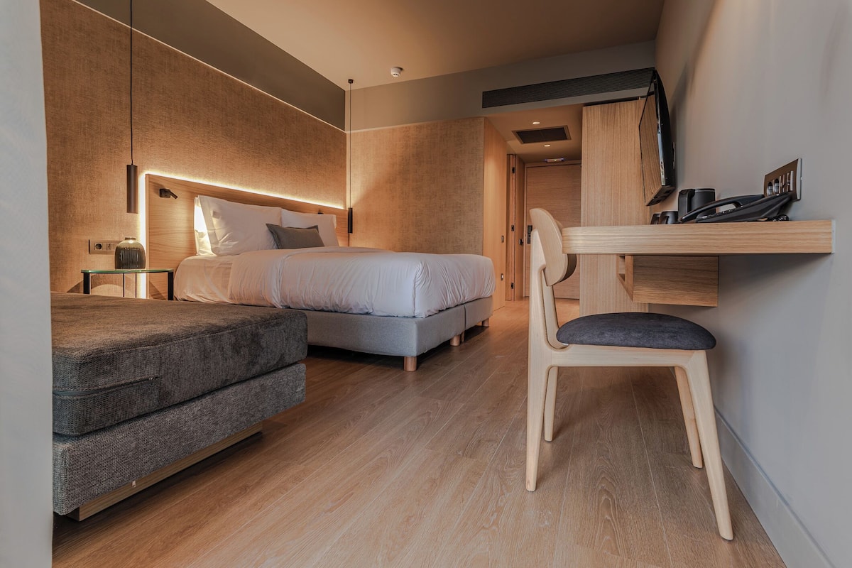 Una habitación de hotel moderna con una cama grande, un escritorio con una silla, un sofá y un televisor montado en la pared.