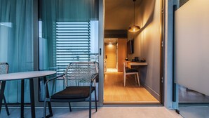 A modern hotel room with a glass door leading to a dining area, a chair, and a table. - Magnes Hotel (Volos)