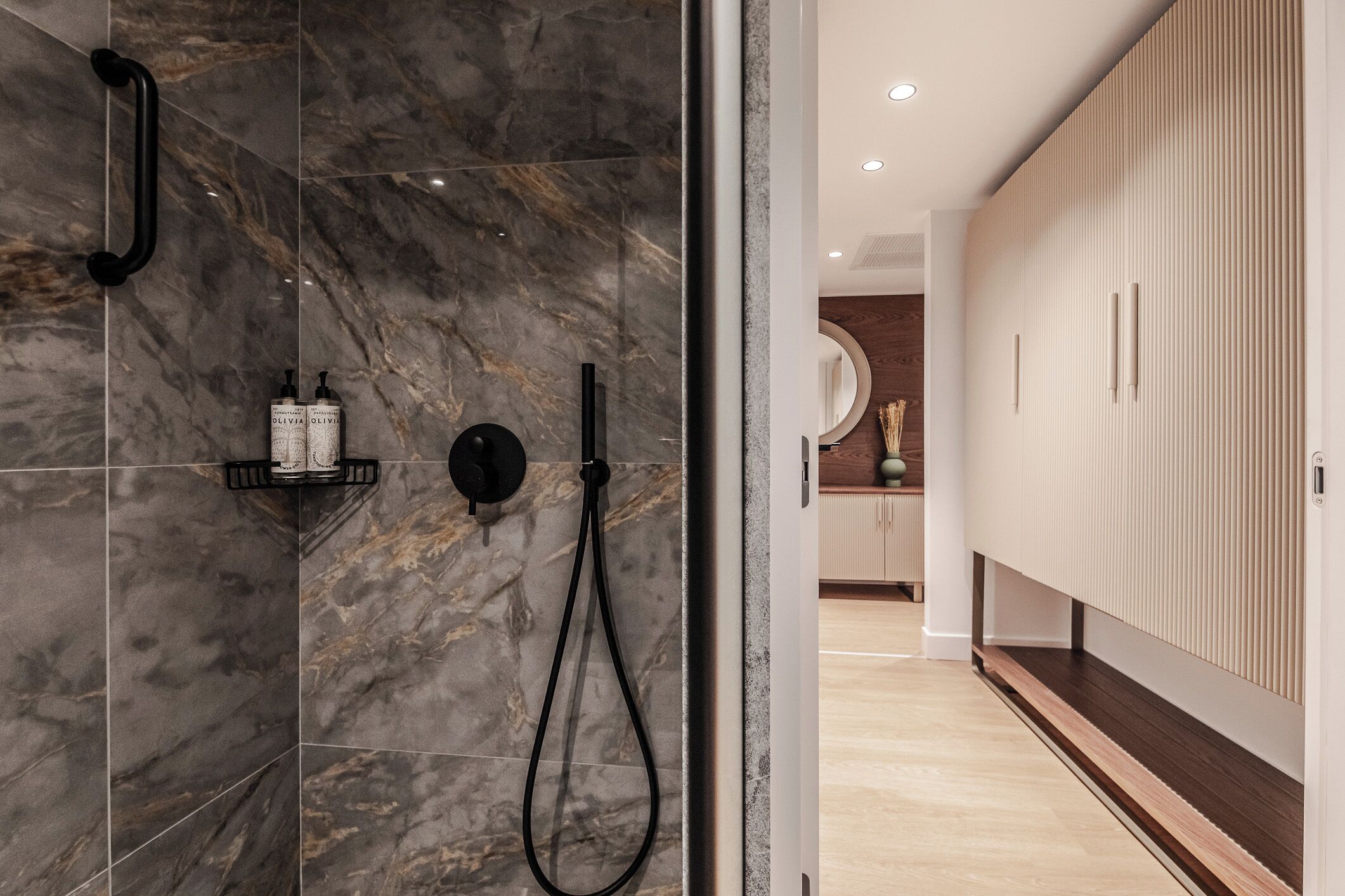 Un baño moderno con baldosas de mármol, zona de ducha y tocador de madera con armarios.