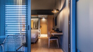 A modern hotel room with a sliding door leading to a bedroom, a desk with a chair, and a bed with curtains.