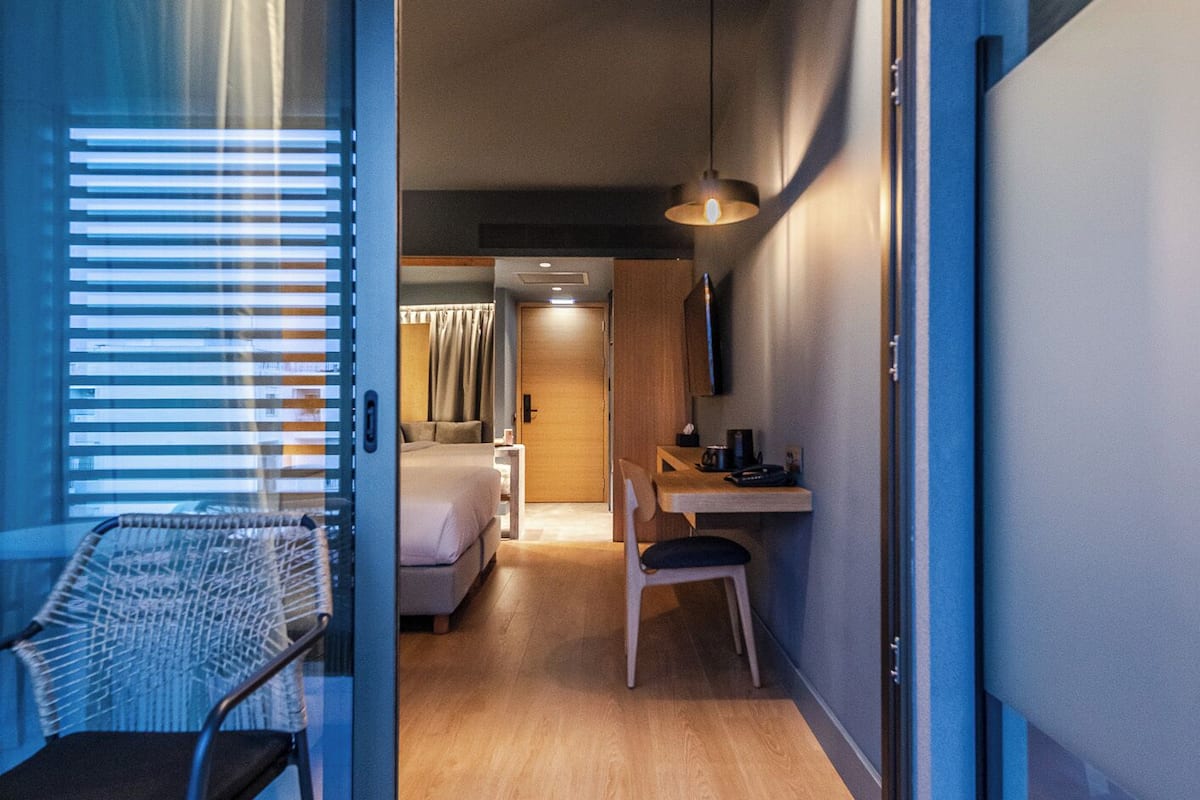 Habitación de hotel moderna con puerta corrediza que da a un dormitorio, un escritorio con silla y una cama con cortinas.