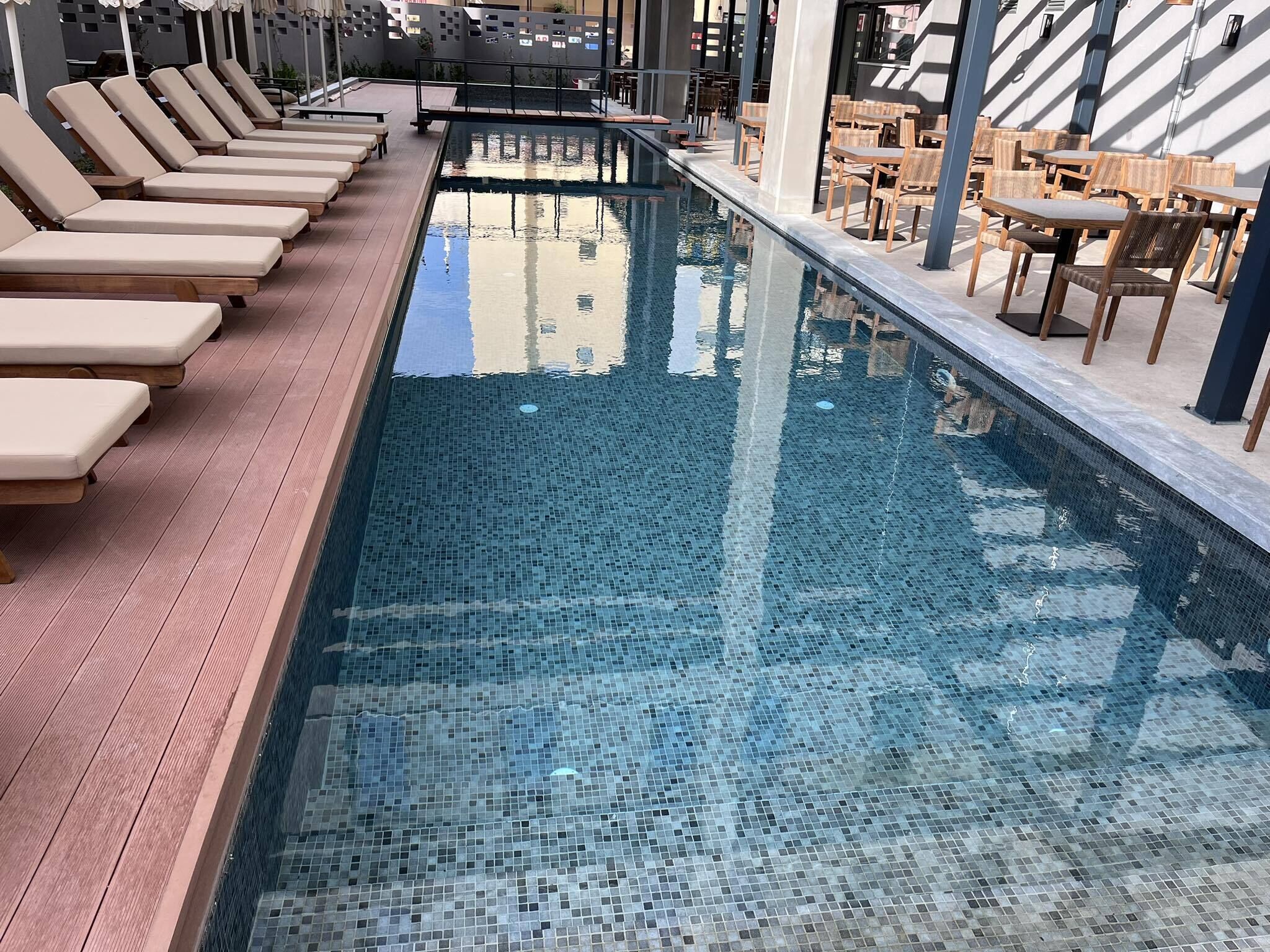 Une piscine entourée de chaises longues et de tables en bois sur la terrasse.