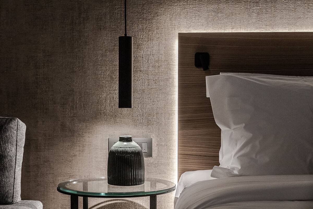 Una habitación de hotel moderna con una mesa redonda de vidrio, una pared con textura y un cabecero de madera.