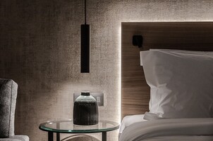 A modern hotel room with a glass table, a textured wall, and a wooden headboard.