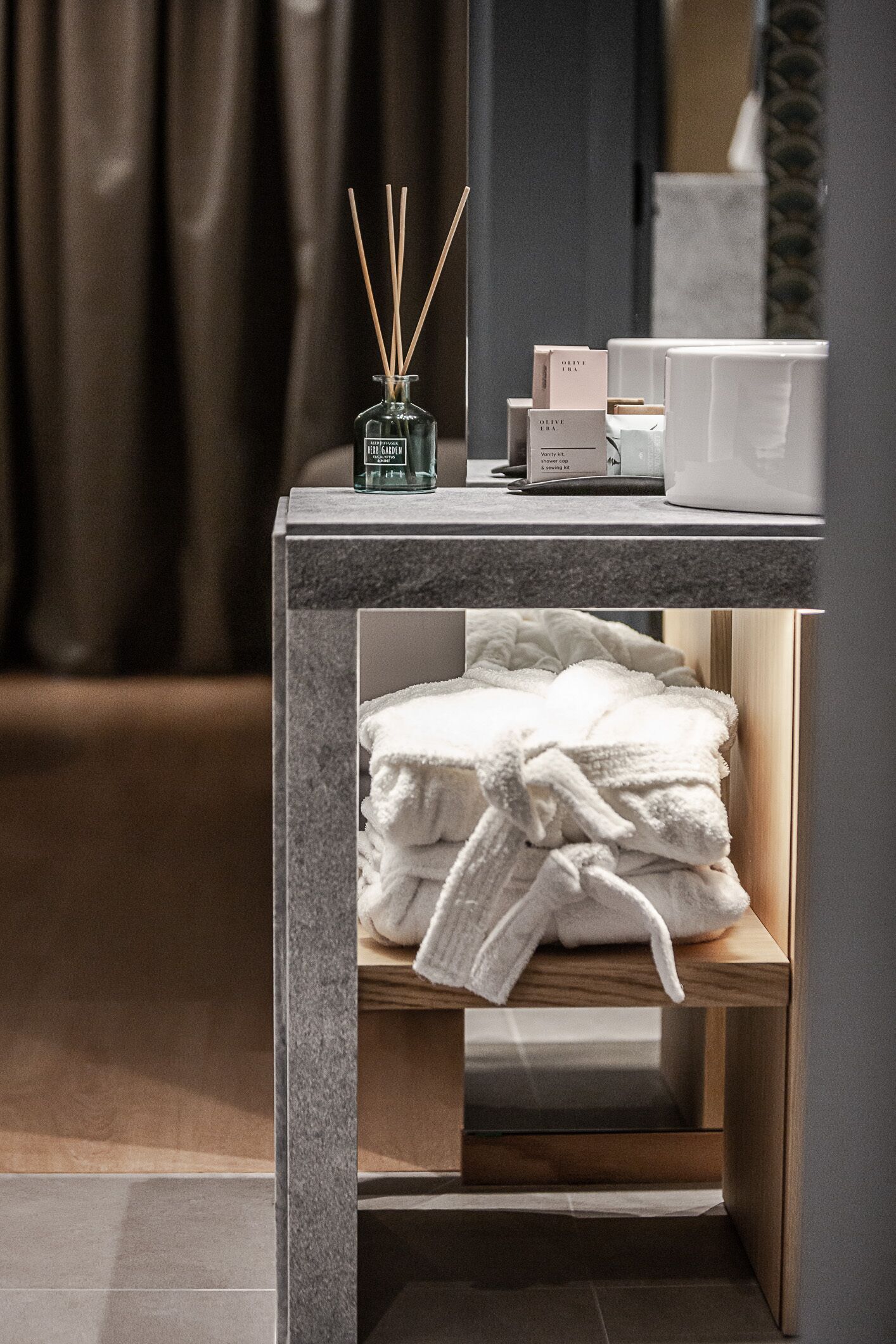 A modern bathroom with a marble countertop, a glass bottle of reed diffuser, a white towel, and a wooden shelf.