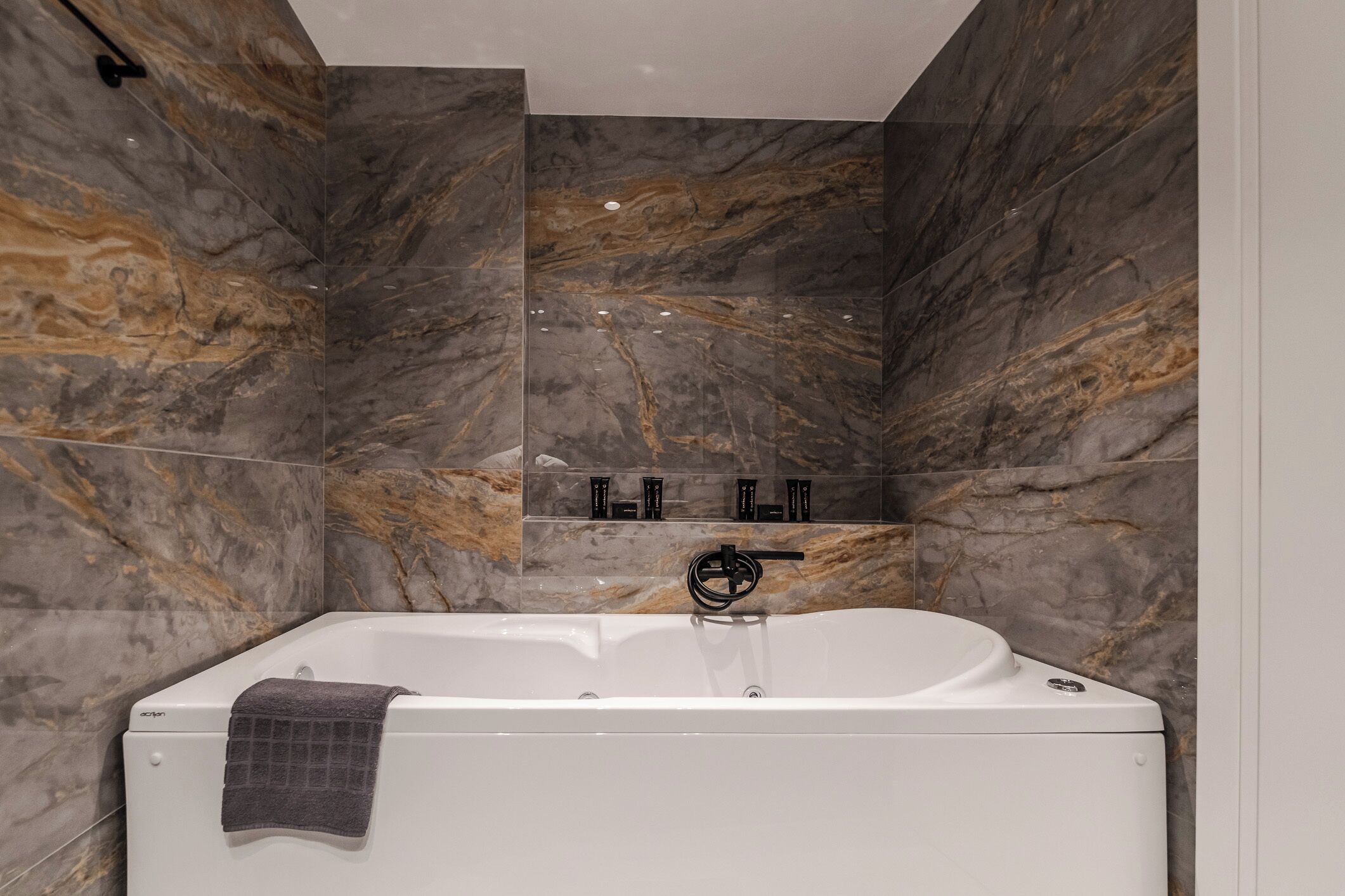 Un baño moderno con una bañera independiente, paredes de mármol y un estante con artículos de aseo.