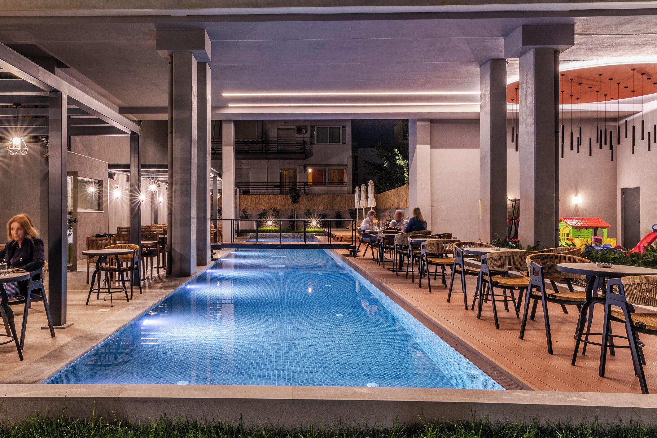 A poolside area with tables and chairs, a pool, and a view of a building in the background.
