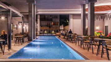A poolside area with tables and chairs, a pool, and a view of a building in the background.