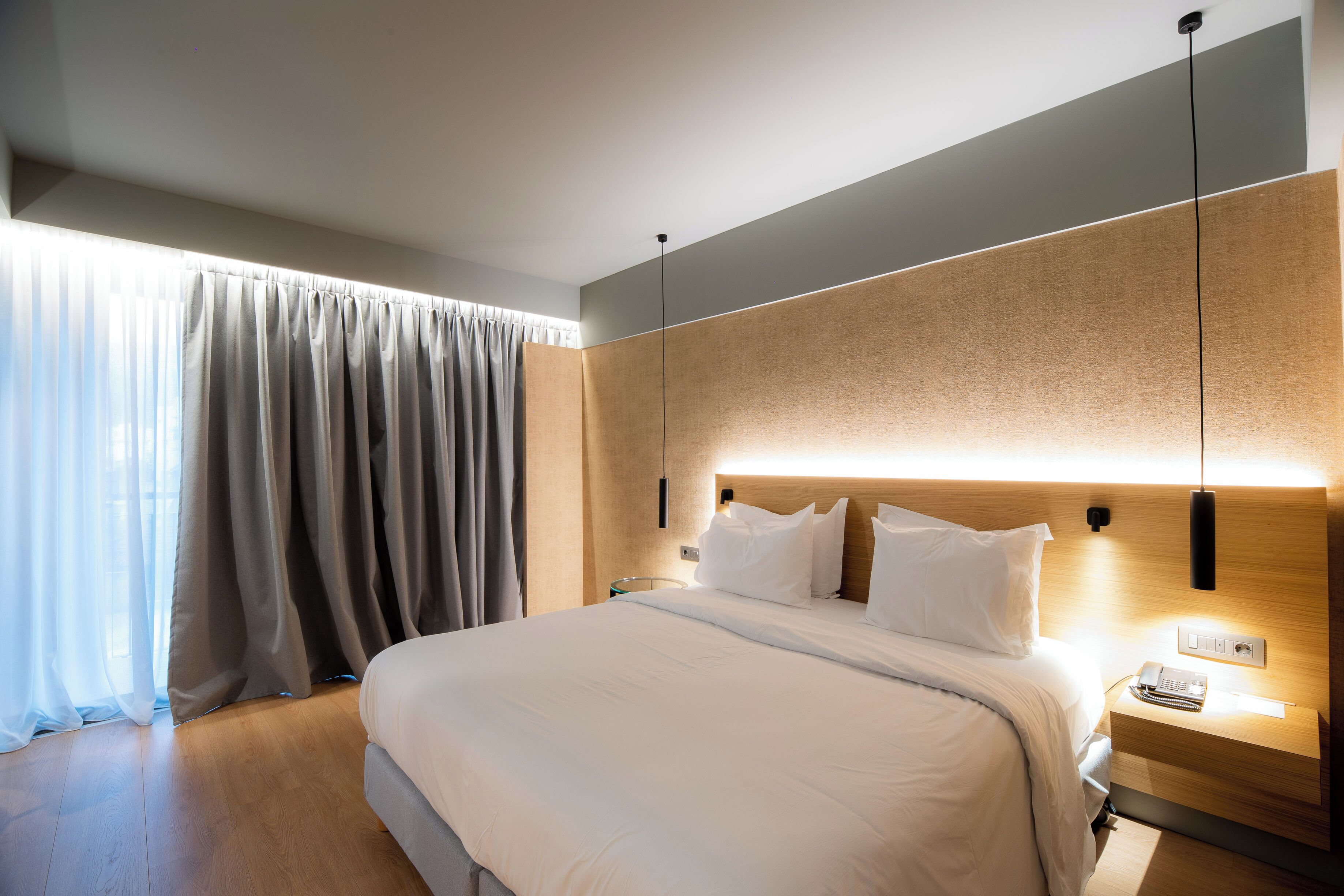 A modern hotel room with a large bed, a bedside table with a lamp, and a view of the city through the window.
