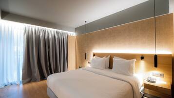 A modern hotel room with a large bed, a bedside table with a lamp, and a view of the city through the window.