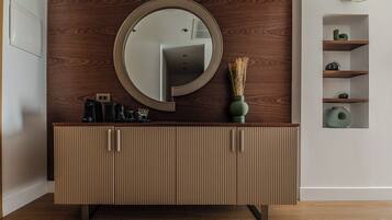 A modern bathroom with a wooden vanity, a round mirror, and a built-in shelf with decorative items.