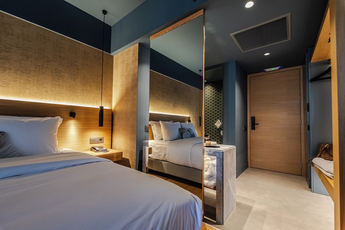 Una habitación de hotel moderna con una cama grande, mesitas de noche, un espejo y un armario.