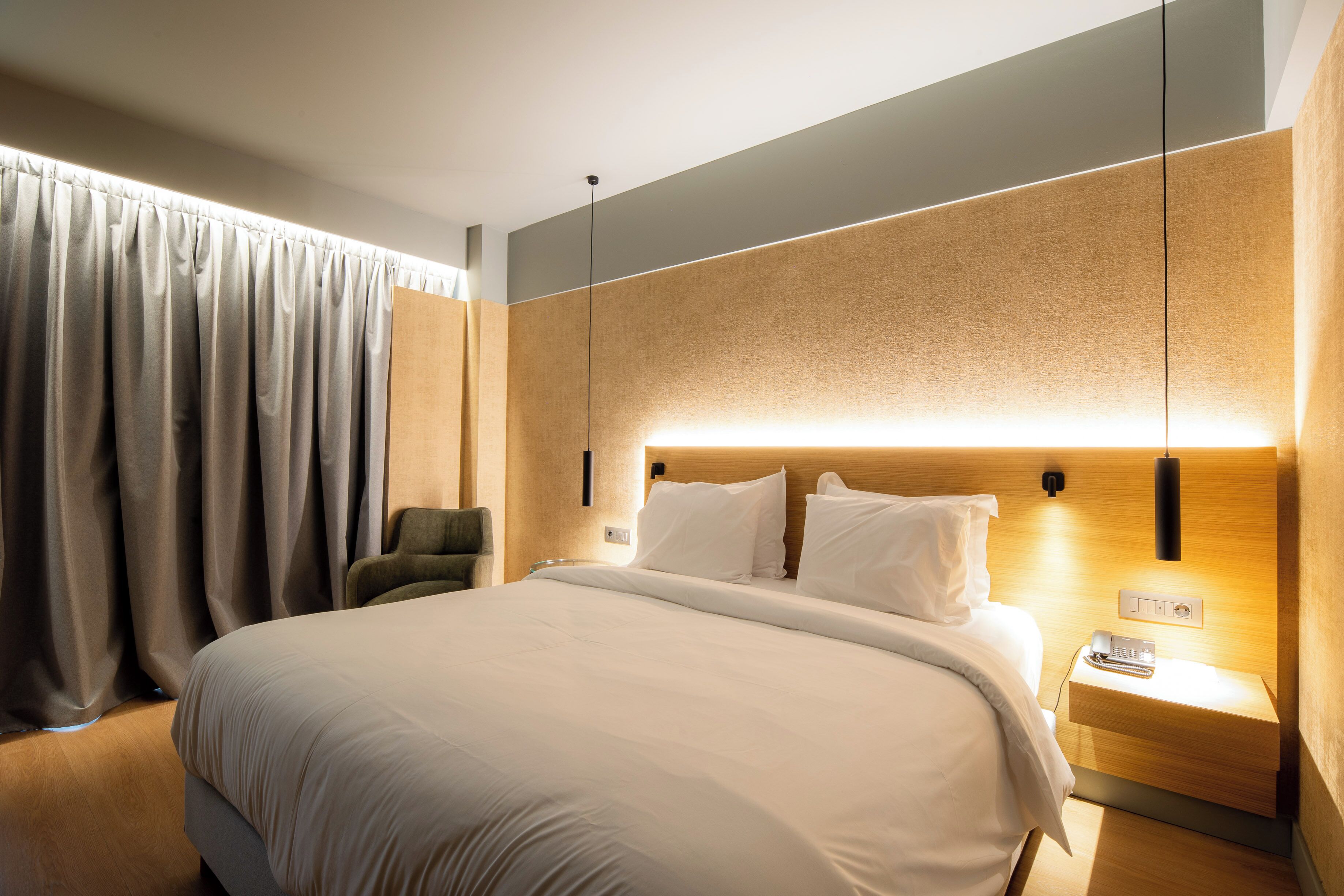 Habitació d'hotel moderna amb un llit gran, una taula de nit amb una làmpada i una cadira.