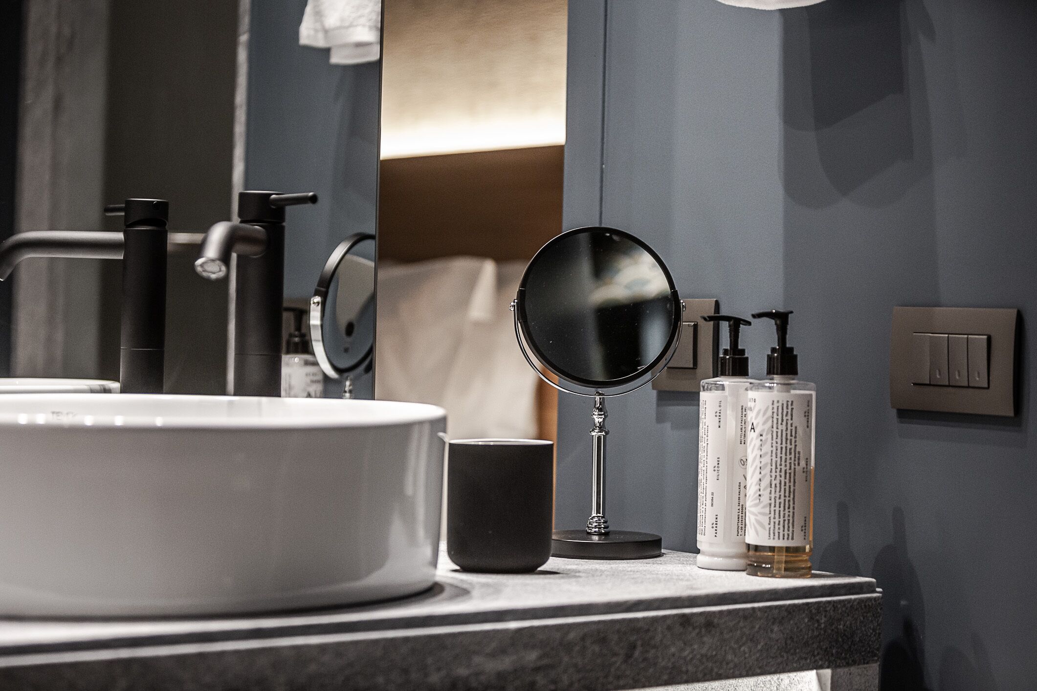 A bathroom vanity with a round mirror, a sink, and toiletries.