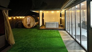 Un área de spa con hidromasaje, sauna de barril de madera y una sala acristalada con vistas.