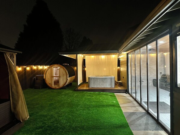 Un espace bien-être comprenant un jacuzzi, un sauna en forme de tonneau en bois et une pièce fermée par des parois de verre offrant une vue panoramique.