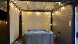 Un jacuzzi con revestimiento de madera, rodeado por una zona cubierta con luces de cadena.