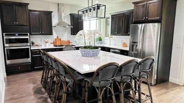 Una cocina moderna con armarios de madera oscura, electrodomésticos de acero inoxidable y una isla central con taburetes de bar.