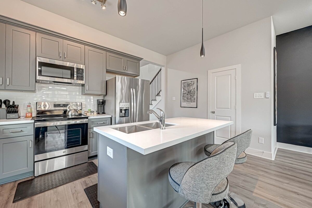 A modern kitchen with stainless steel appliances, grey cabinetry, and a central island with bar stools.