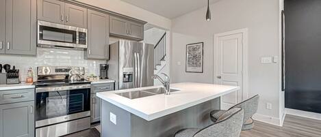 A modern kitchen with stainless steel appliances, grey cabinetry, and a central island with bar stools.