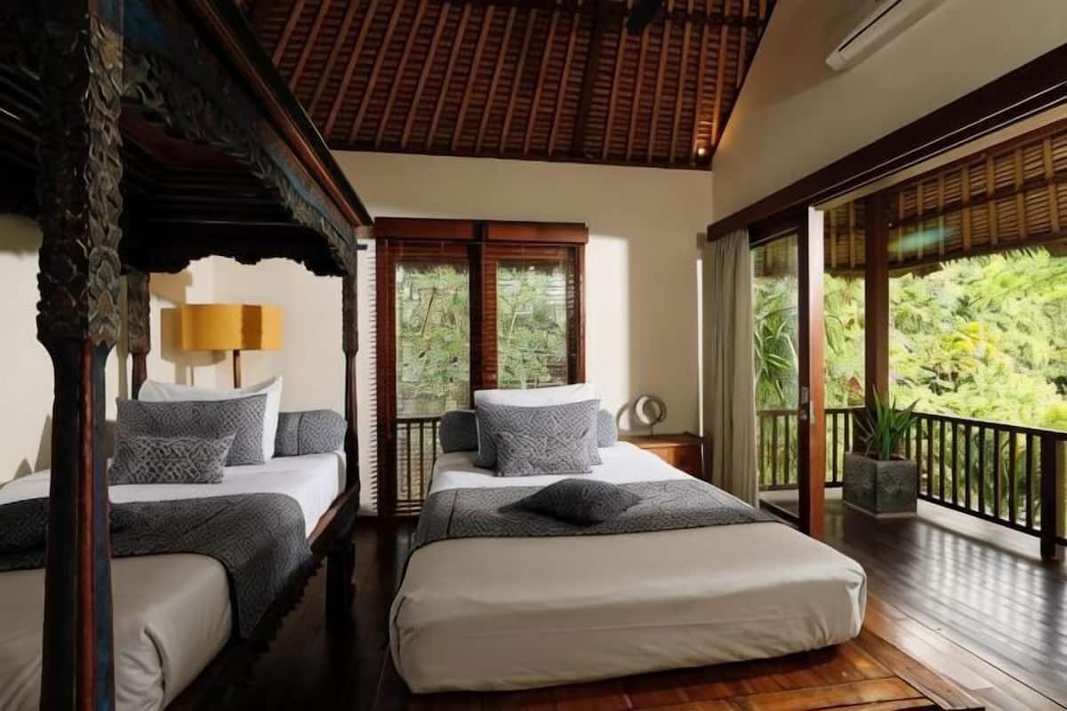 A bedroom with two beds, a balcony, and a view of greenery.