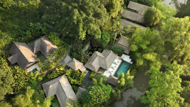 Une vue aérienne d’un complexe hôtelier comprenant plusieurs bungalows aux toits de chaume, une piscine centrale et une végétation luxuriante qui entoure l’ensemble du site.