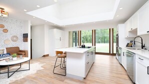 A modern kitchen with a central island, white cabinetry, and a large window offering a view of the outdoors.