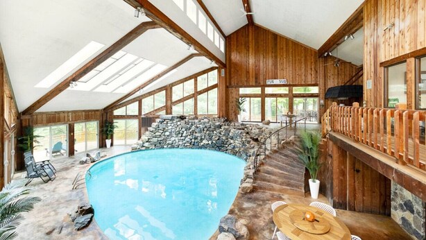 A large indoor swimming pool with a stone wall, wooden beams, and a sun sign.