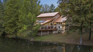 A lakeside lodge with a large deck, a second-story balcony, and a reflection in the water.