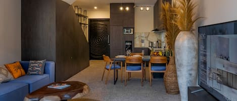 A modern living room with a dark wood accent wall, a blue sofa, a coffee table, and a dining area with chairs and a table.