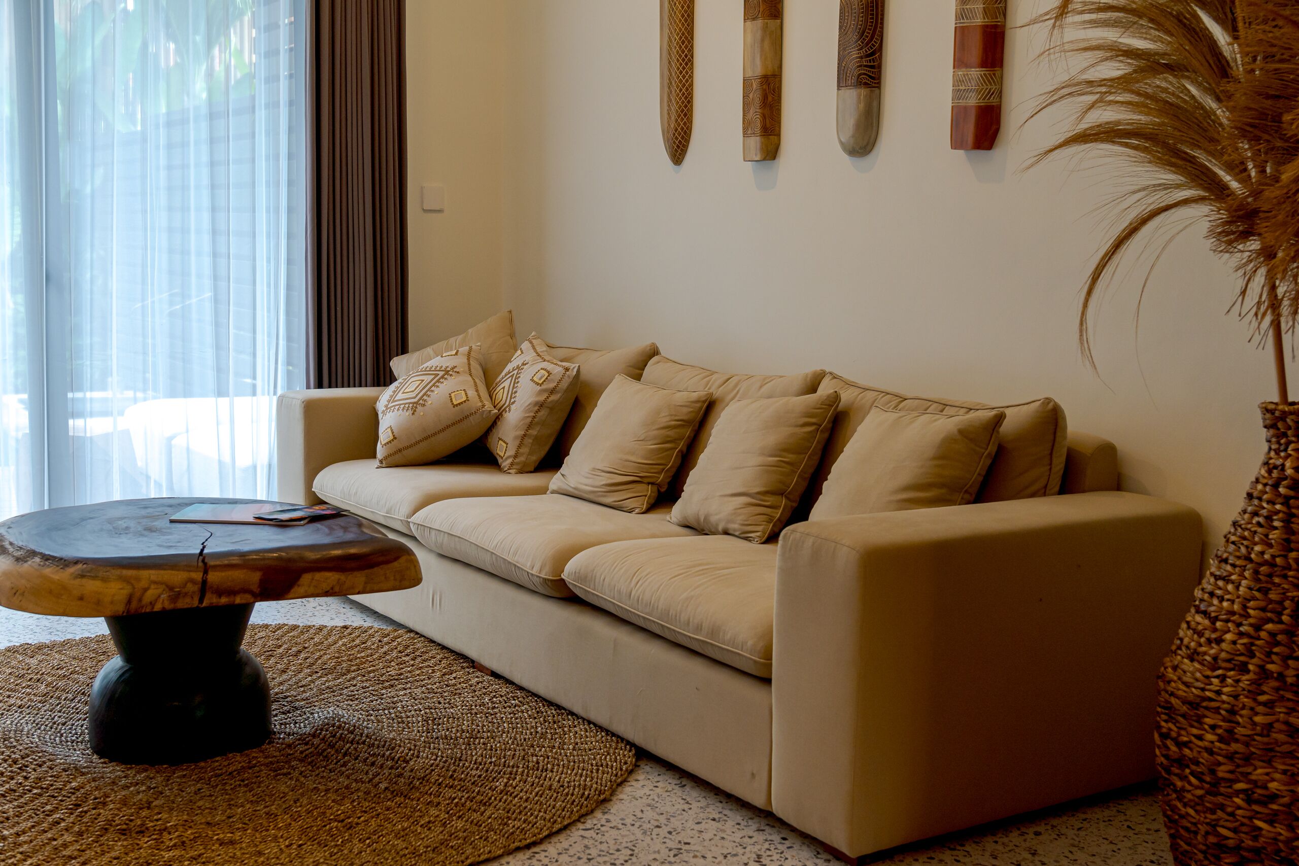 Ein Wohnzimmer mit einem beigen Sofa, einem runden Couchtisch und einem gewebten Teppich.
