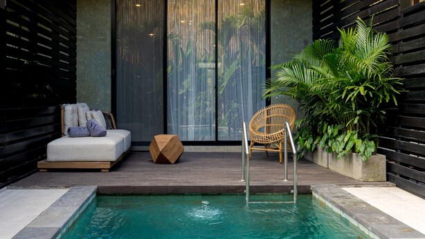 A pool area with a lounge chair, a wooden stool, and a wicker chair. - Sunny Village Batu Bolong (Canggu)