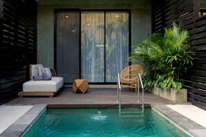 Zona de piscina con una silla de reposo, un taburete de madera y una silla de mimbre.