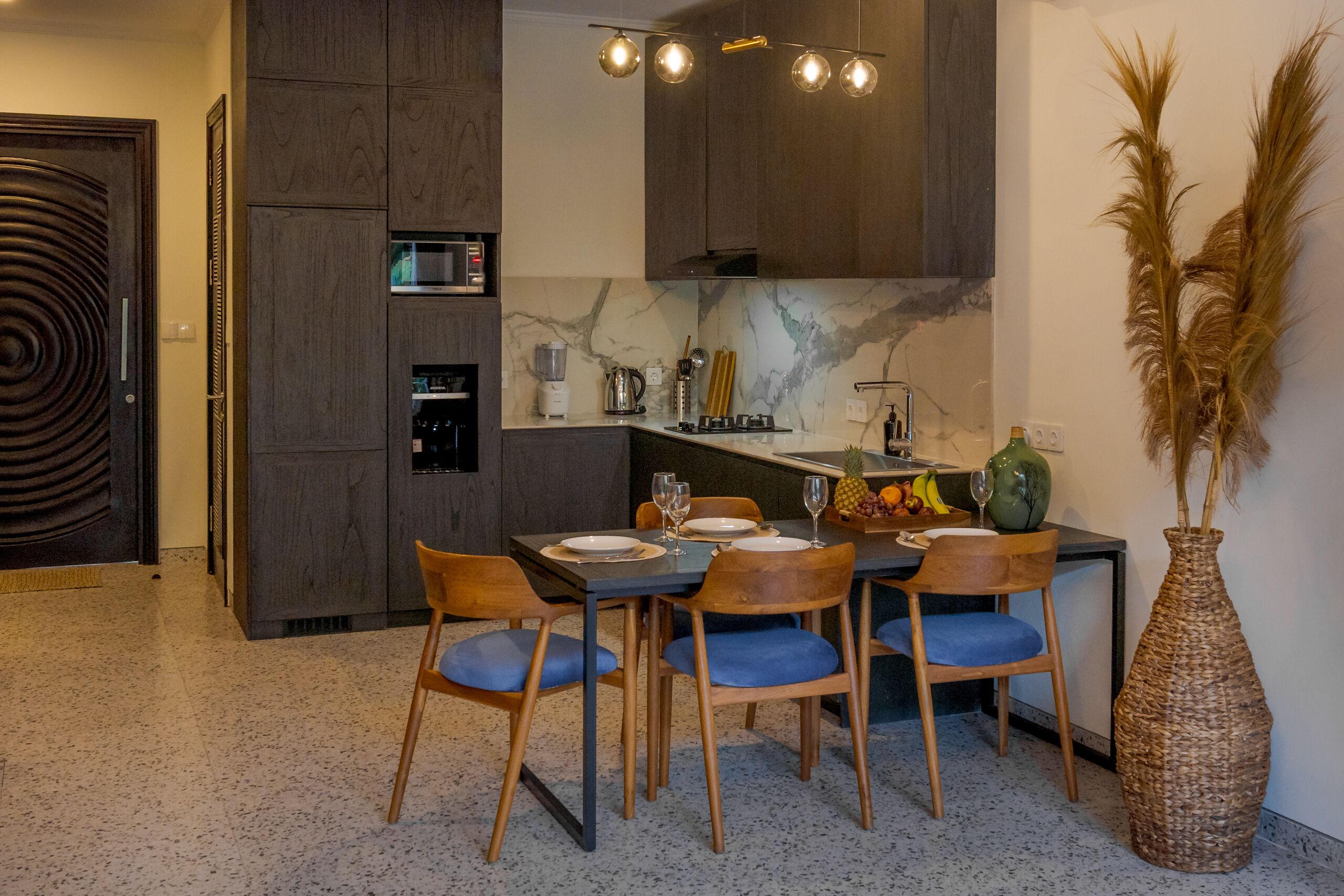Eine moderne Küche mit dunklen Holzschränken, einer Marmor-Spritzschutzwand und einem Essbereich mit Holzsesseln und einem Tisch für vier Personen.