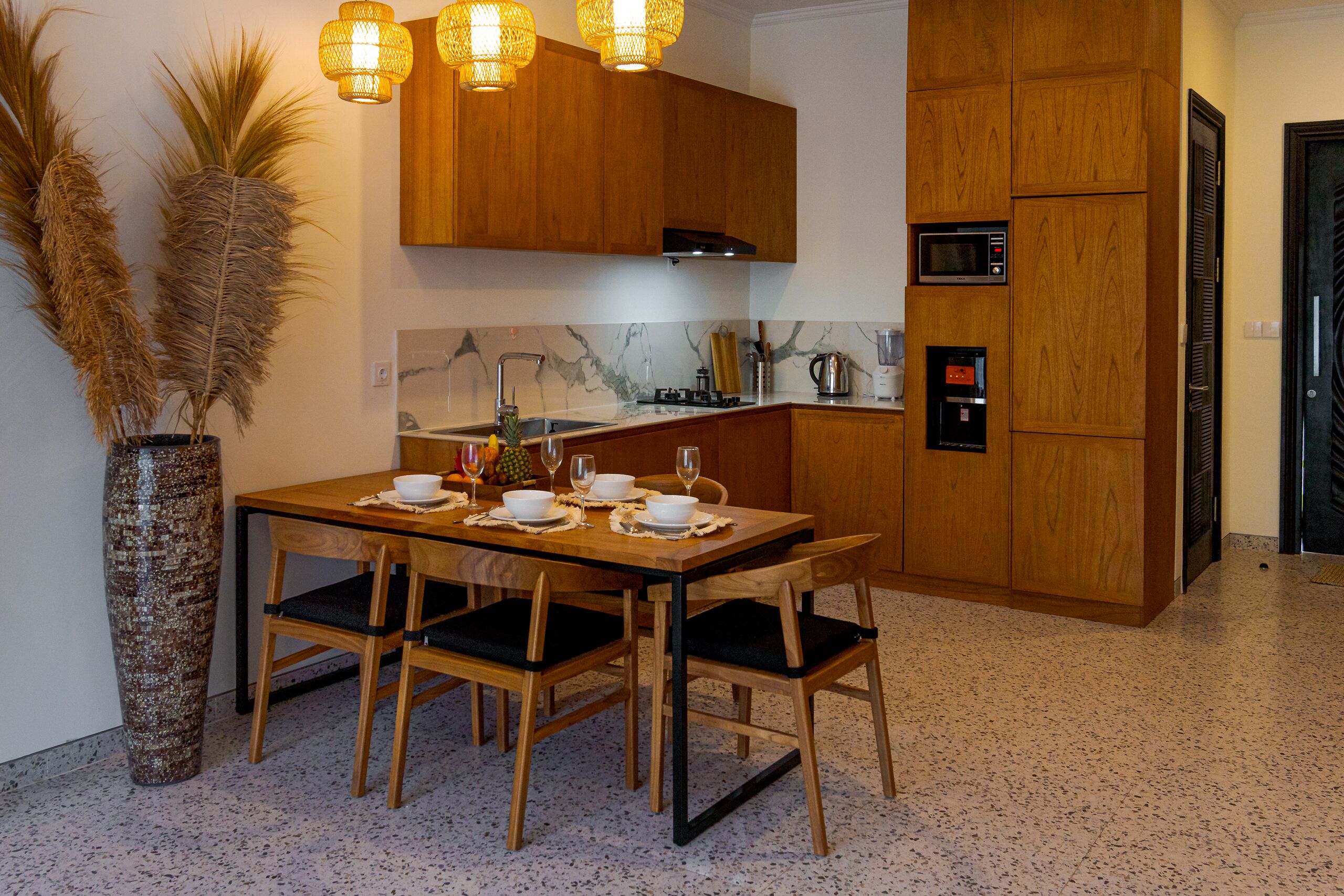 A modern kitchen with wooden cabinets, a marble backsplash, and a dining area set with a table and chairs.