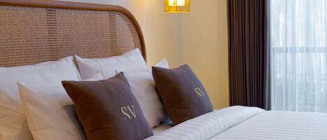Una cama bien tendida con almohadas blancas y marrones, un cabecero tejido y una lámpara de pared.