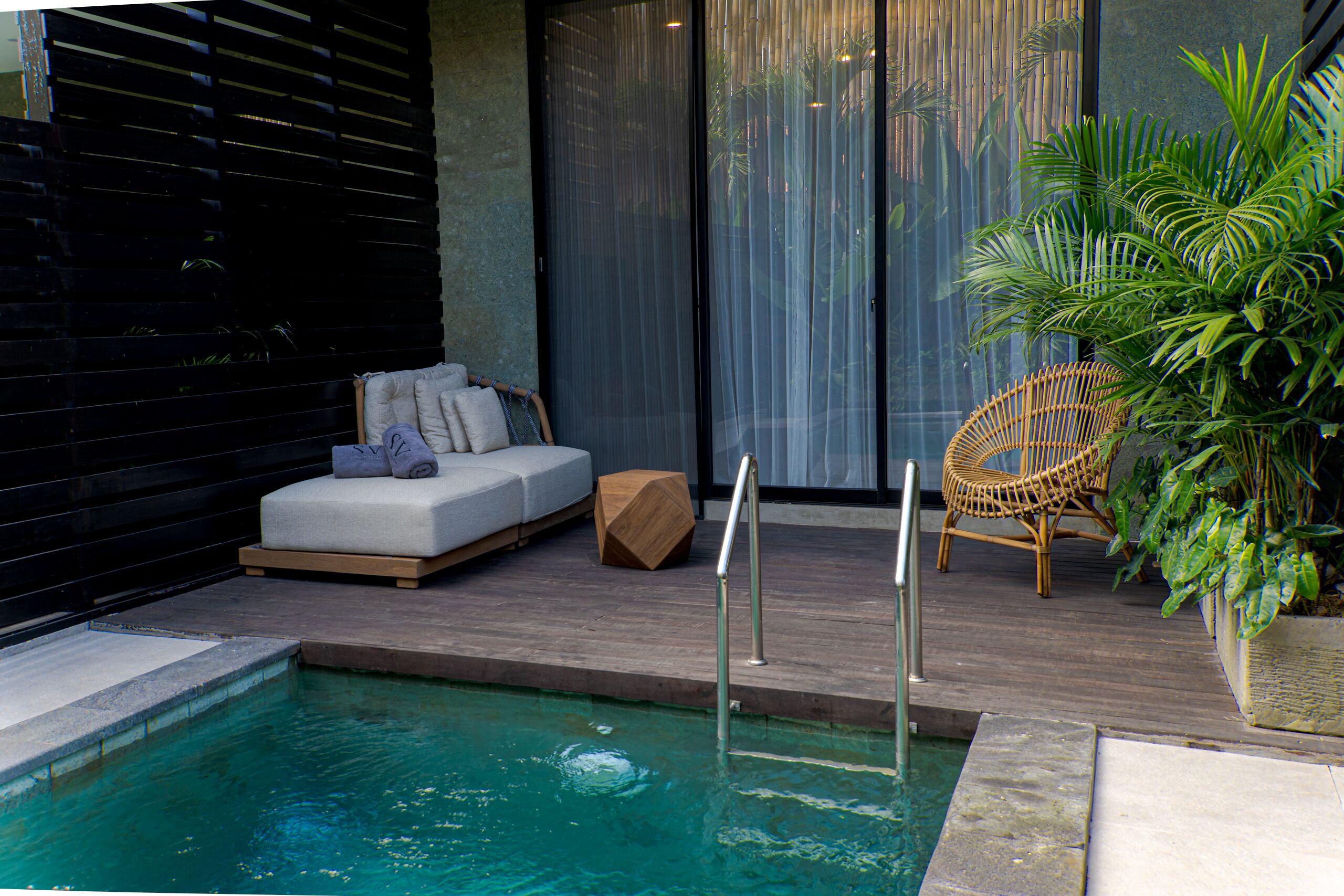 Un espace piscine extérieur moderne, doté d’un coin salon, d’une terrasse en bois et d’un fauteuil en osier.