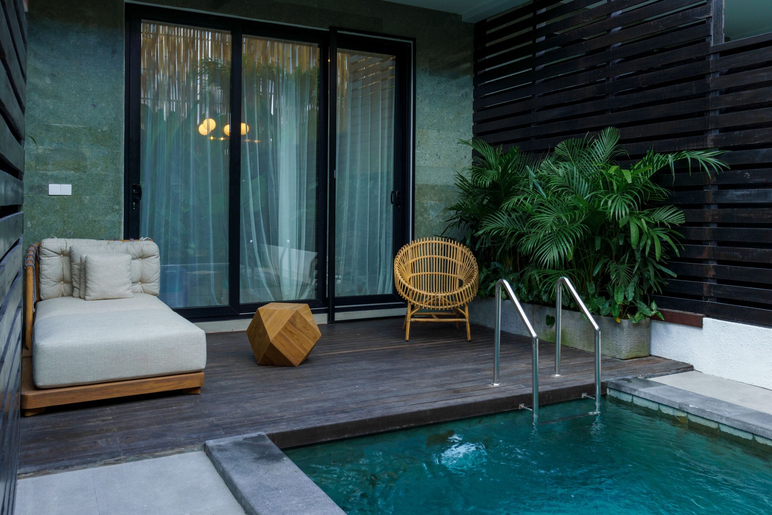 A modern outdoor pool area with a sofa, a chair, and a potted plant.