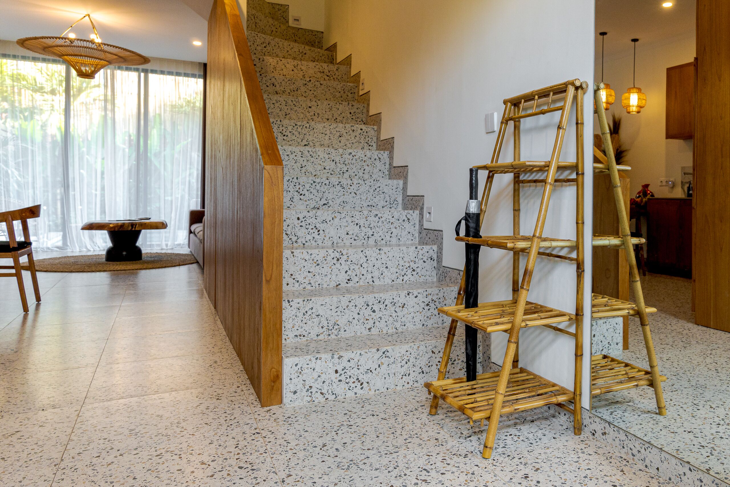 Un escalier avec une rampe en bois, une étagère en bambou et un coin repas avec des chaises et une table.
