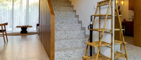 A staircase with a wooden handrail, a bamboo shelf, and a dining area with chairs and a table.