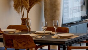 A dining table set with plates, cutlery, and wine glasses, with a large vase and a tall plant in the background. - Sunny Village Batu Bolong (Canggu)