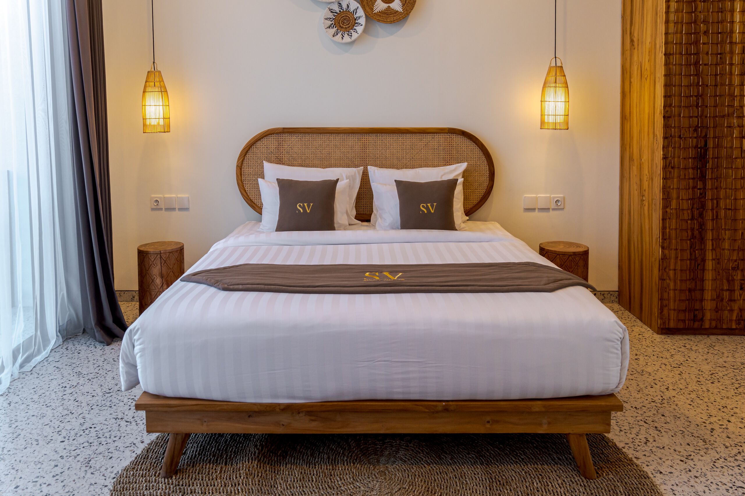 A neatly made bed with a wooden headboard, two bedside tables, and two wall-mounted lamps.