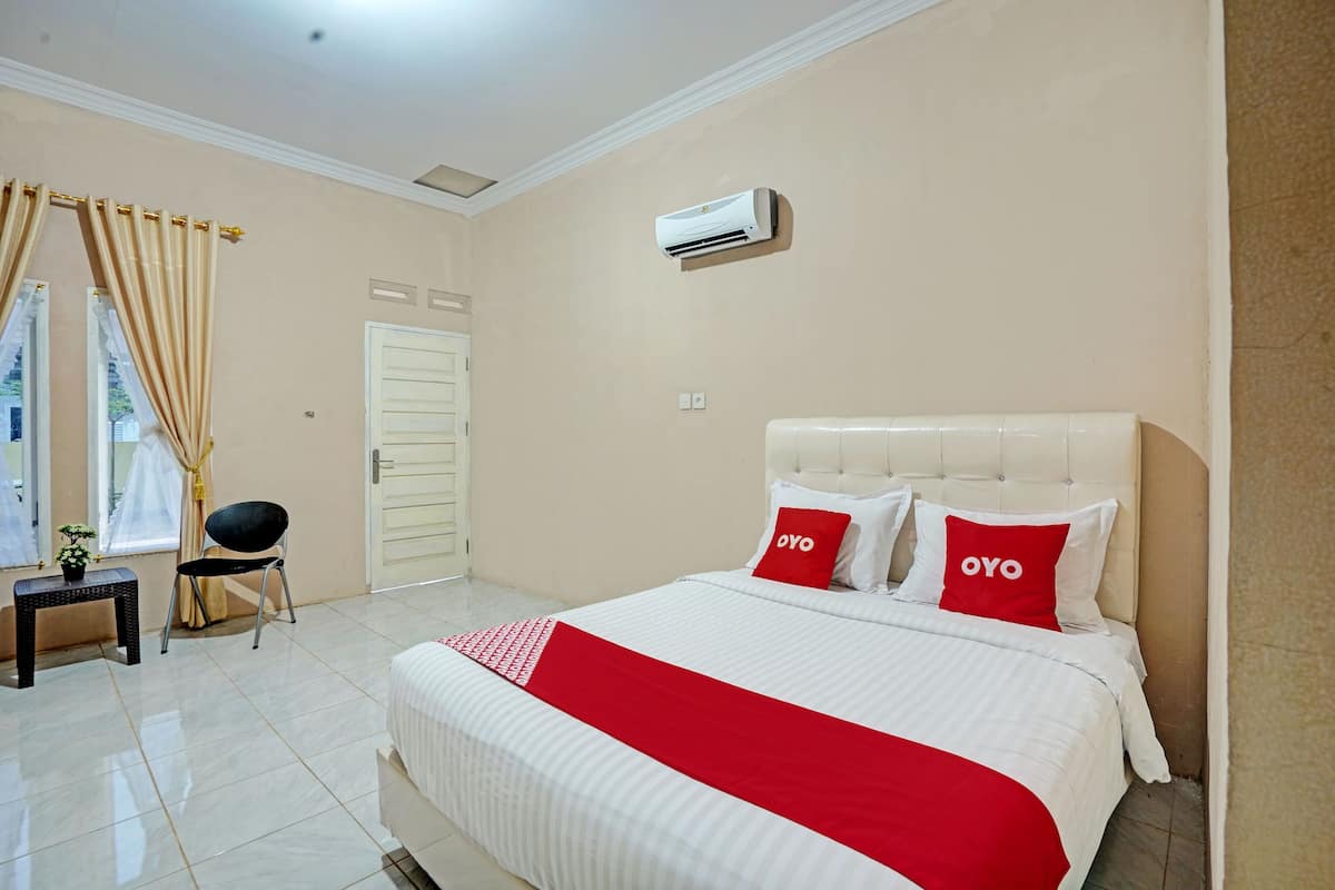 Habitación de hotel con una cama grande, dos almohadas con la palabra "OYO" y una mesita con una silla, además de un equipo de aire acondicionado en la pared.