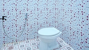 A bathroom with a polka dot tile pattern on the walls and floor, a toilet, and a shower with a hose.