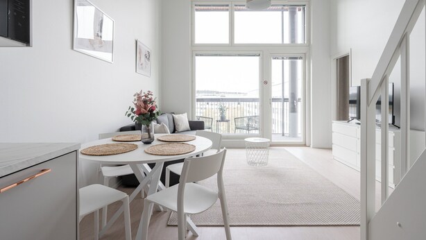 Een moderne, goed verlichte eetruimte met een witte tafel, stoelen en een bloevas.